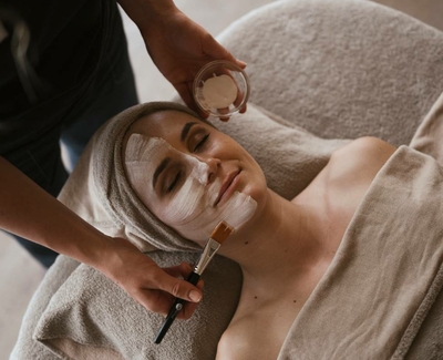 A woman receives a facial treatment with cream and a brush in the spa area.