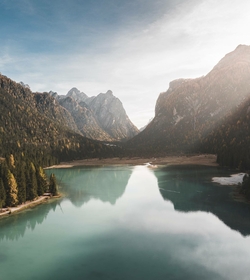 Ein ruhiger Bergsee liegt zwischen bewaldeten Hängen und steilen Gipfeln in den Alpen.
