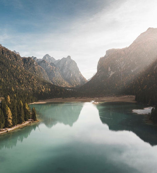 Ein ruhiger Bergsee liegt zwischen bewaldeten Hängen und steilen Gipfeln in den Alpen.