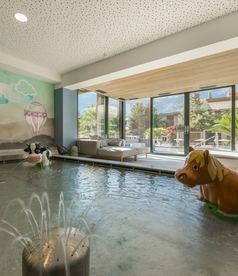 Family Spa mit Innenpool im Feldhof Ein Innenpool mit Springbrunnen, Sitzbereich und verspielten Tierfiguren vor großen Fenstern.