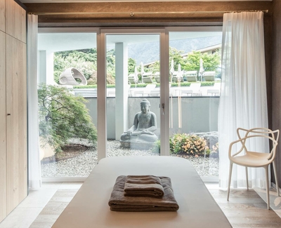 Ein Ruheraum mit Liege, Buddhafigur und Blick in den Garten durch große Schiebetüren.