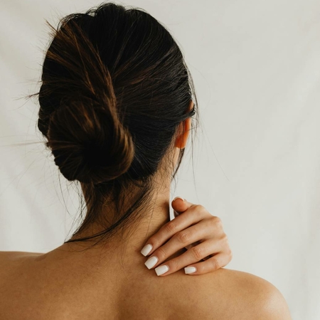 Una donna con i capelli raccolti tocca la spalla durante un trattamento benessere nella spa.