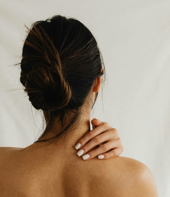 Beauty Treatment im Spa des Feldhof Eine Frau mit hochgestecktem Haar berührt im Spa ihre Schulter während einer Wellnessbehandlung.