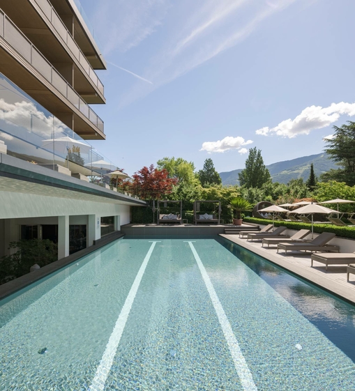Una piscina a sfioro con lettini e ombrelloni si trova accanto all'hotel con vista sulle montagne.