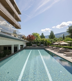 Una piscina a sfioro con lettini e ombrelloni si trova accanto all'hotel con vista sulle montagne.