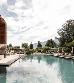 Una piscina all’aperto con lettini e vista sulle montagne in un wellness hotel a Naturno.