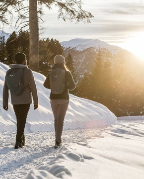 Winterwandern im Meraner Land Zwei Personen wandern auf einem verschneiten Weg mit Blick auf die Berge im Winterlicht.