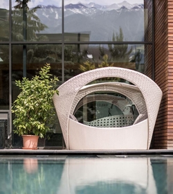 Una poltrona lounge imbottita è posizionata a bordo piscina davanti a una vetrata con vista sulle montagne.