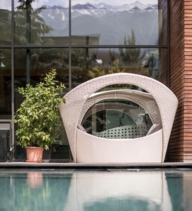 Una poltrona lounge imbottita è posizionata a bordo piscina davanti a una vetrata con vista sulle montagne.