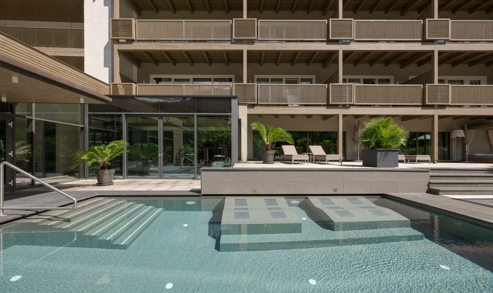 Una piscina esterna con lettini e piante davanti alla facciata dell’hotel.