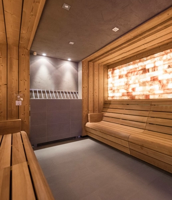 Sauna im Wellnesshotel in Naturns Holzsauna mit langen Sitzbänken und beleuchteter Salzwand im Wellnessbereich.