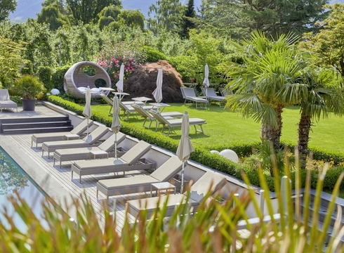 Un curato giardino wellness con lettini, ombrelloni e area piscina immersa nel verde.