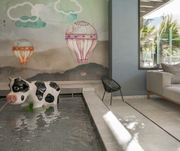 Ein kleiner Pool mit Kuh-Sitzfigur steht vor einer Wandmalerei mit Heißluftballons und Wolken.