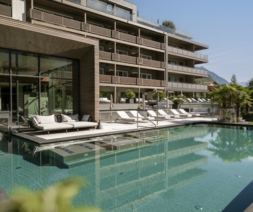 Der Außenpool liegt vor dem modernen Wellnesshotel mit Liegen und Glasfront.