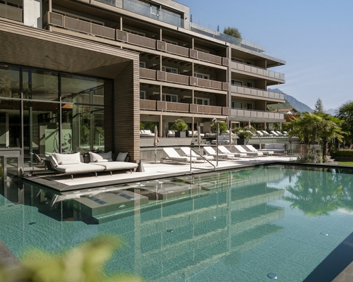 Der Außenpool liegt vor dem modernen Wellnesshotel mit Liegen und Glasfront.