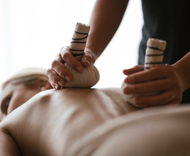 Massage im Wellnesshotel Feldhof in Naturns Eine Massage mit warmen Kräuterstempeln auf dem Rücken in einem Wellnessbereich.