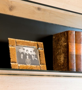 Ein dekoratives Bücherregal mit gerahmtem Schwarzweißfoto und antiken Büchern steht vor einer dunklen Rückwand.