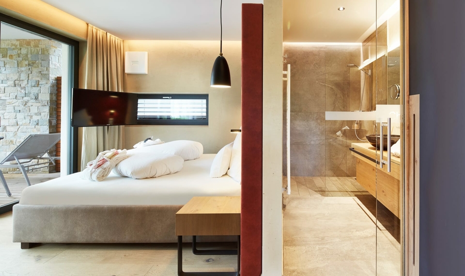 Chalet mit Schlafzimmer und Bad im Feldhof Ein modernes Chalet-Schlafzimmer mit großem Bett und Blick ins Badezimmer mit Glaswand.