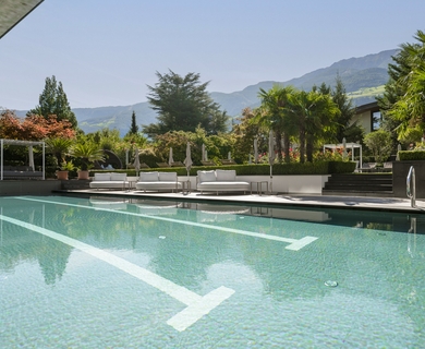 Pool im Wellnesshotel in Naturns Der Außenpool liegt vor Liegen, Palmen und Bergen im Feldhof DolceVita Resort in Naturns.
