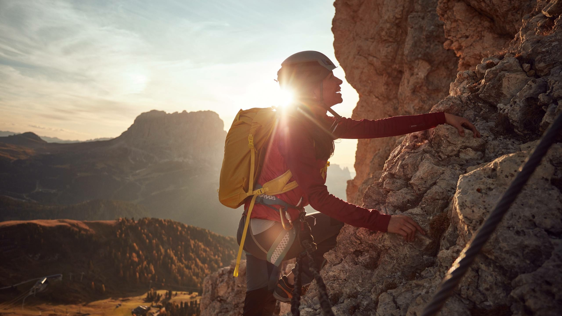 Eine Kletterin mit gelbem Rucksack steigt bei Sonnenuntergang an einer Felswand auf.