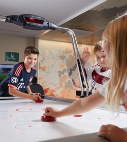 Drei Kinder spielen an einem Air-Hockey-Tisch im Innenbereich.