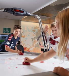 Drei Kinder spielen an einem Air-Hockey-Tisch im Innenbereich.