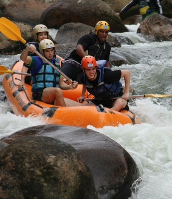 Rafting mit Familie in den Bergen Vier Personen fahren in einem orangefarbenen Raft durch wildes Wasser zwischen Felsen.