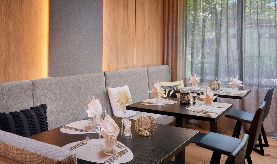 Ein moderner Restaurantbereich mit gedeckten Tischen, Eckbank und großen Fenstern im Feldhof DolceVita Resort.