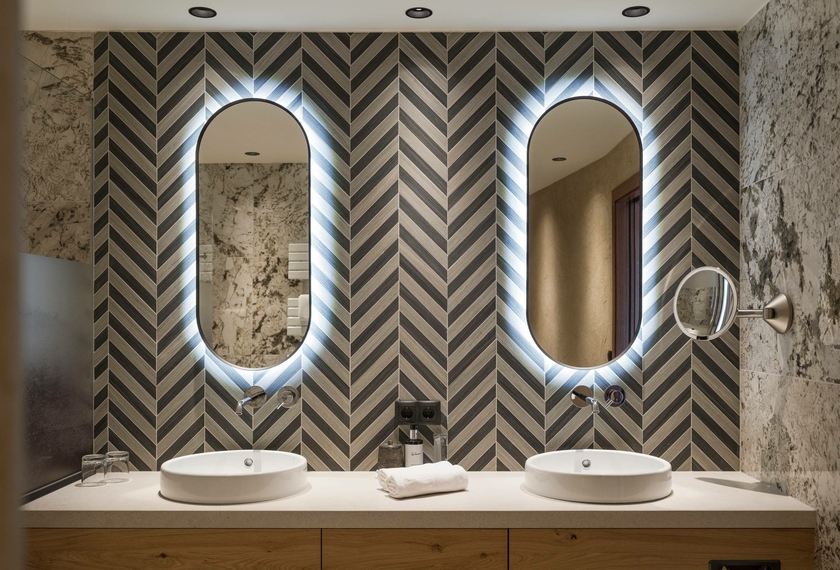Badezimmer mit Doppelwaschtisch in der Suite Ein Badezimmer mit zwei Waschbecken, zwei ovalen Spiegeln und gemusterten Wänden.