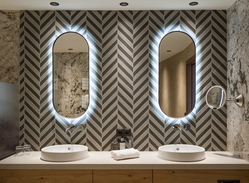 Badezimmer mit Doppelwaschtisch in der Suite Ein Badezimmer mit zwei Waschbecken, zwei ovalen Spiegeln und gemusterten Wänden.
