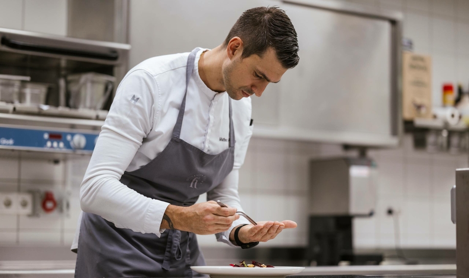 A chef from the kitchen team carefully plates a dish in the hotel restaurant.