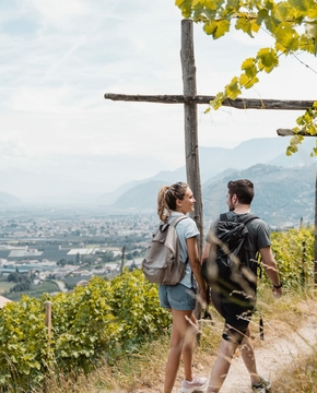 Zwei Wanderer stehen auf einem Weg am Weinberg und blicken über das Tal bei Naturns.