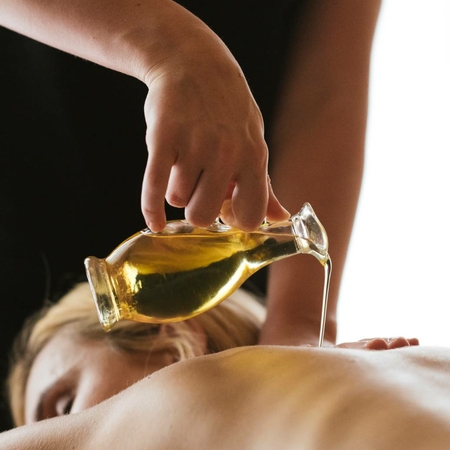 Una mano versa olio caldo sulla schiena di una persona sdraiata durante un massaggio nella spa.