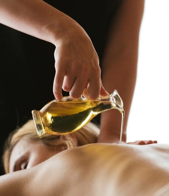 Öl-Massage im Spa des Feldhofs Eine Hand gießt warmes Öl auf den Rücken einer liegenden Person bei einer Massage im Spa.