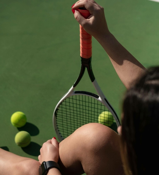 A person holds a tennis racket and several yellow tennis balls on the court.