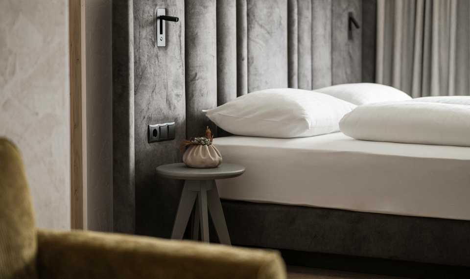 Ein schlichtes Hotelzimmer mit Doppelbett, Beistelltisch und Vorhang in ruhigen Naturtönen.