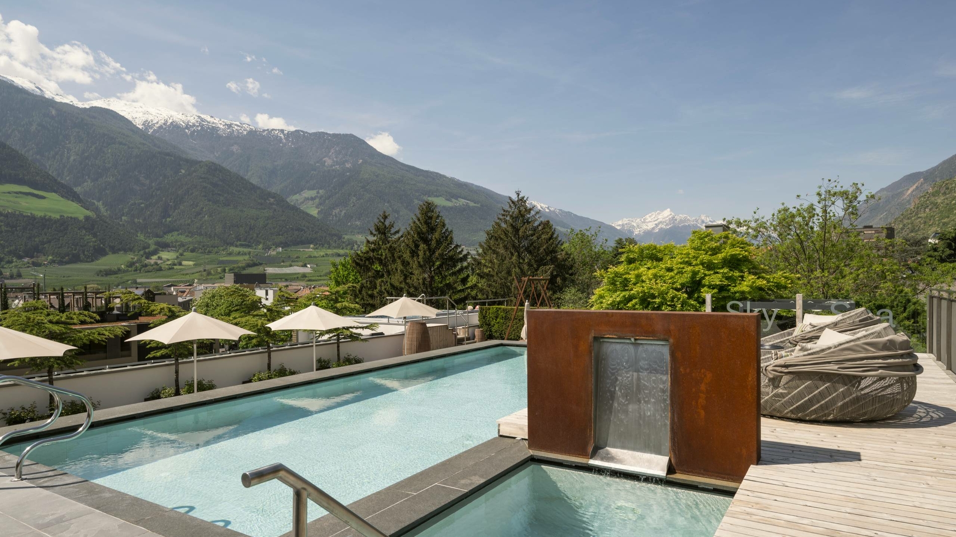 Una piscina esterna con cascata e vista sulle montagne sulla terrazza dell’hotel.