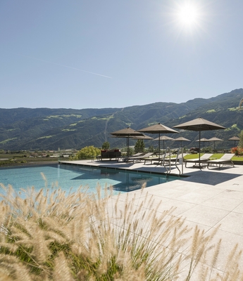 Poolbereich im Wellnesshotel in Naturns Ein Außenpool mit Liegen, Sonnenschirmen und Bergblick im Wellnesshotel.