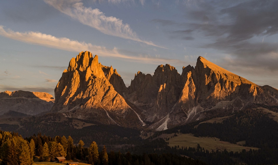 Die Dolomiten leuchten im Abendlicht über bewaldeten Hängen und einer weiten Talfläche.