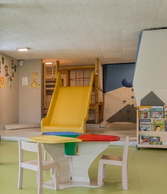 Kinderbetreuung mit Spielbereich im Feldhof Ein heller Spielraum für Kinder mit Rutsche, Tischen, Sitzkissen und großen Fenstern.