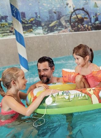 Zwei Kinder und ein Mann spielen im Innenpool mit einem aufblasbaren Ring im Family Spa.