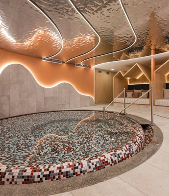 Ruheraum im Spa mit Mosaikbecken Ein Ruheraum im Spa mit rundem Mosaikbecken, Liegen und warm beleuchteter Holzverkleidung.