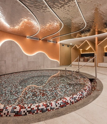 Ruheraum im Spa mit Mosaikbecken Ein Ruheraum im Spa mit rundem Mosaikbecken, Liegen und warm beleuchteter Holzverkleidung.