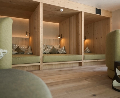 Ruhebereich im Wellnesshotel in Naturns Ein gemütlicher Ruhebereich mit drei Holz-Nischen, grünen Liegen und warmem Licht im Feldhof DolceVita Resort.
