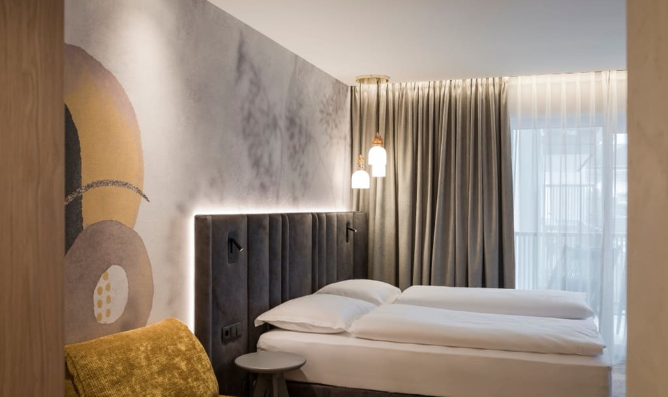 Doppelzimmer La Vita im Feldhof in Naturns Ein modernes Doppelzimmer mit gepolstertem Kopfteil, Bett, Vorhängen und Kuschelecke.