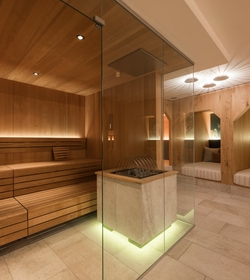 Eine warme Sauna im Family Spa mit Holzvertäfelung, Glasofen und Liegen in einer ruhigen Relaxzone.