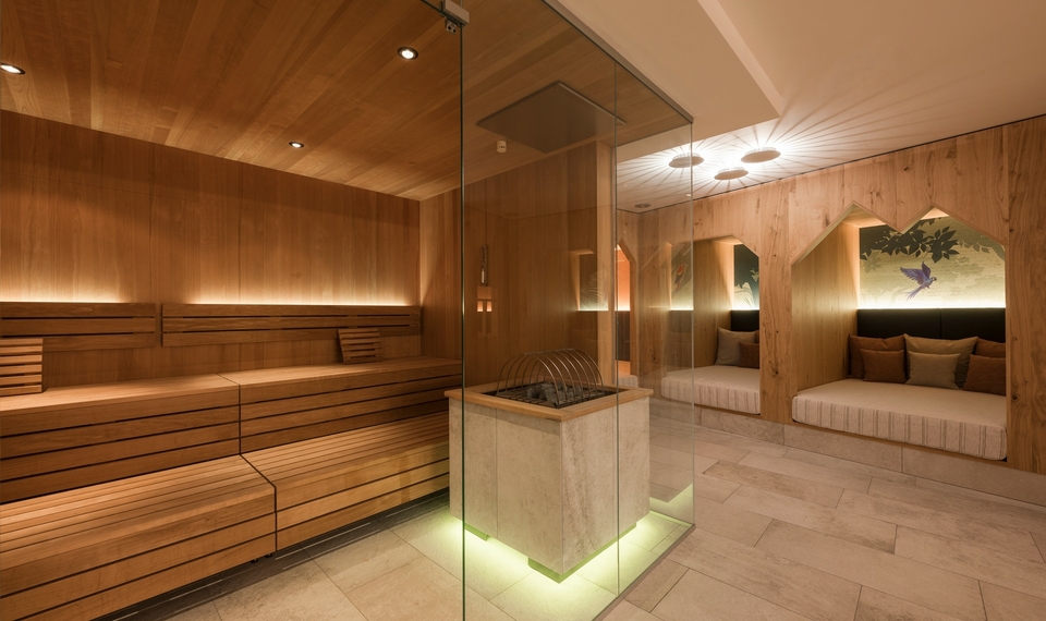 Eine warme Sauna im Family Spa mit Holzvertäfelung, Glasofen und Liegen in einer ruhigen Relaxzone.