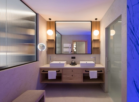 Un bagno moderno della suite con doppio lavabo, mobile in legno e specchi in luce calda.