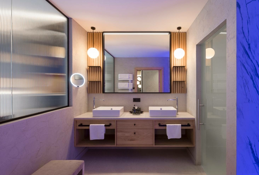 Un bagno moderno della suite con doppio lavabo, mobile in legno e specchi in luce calda.
