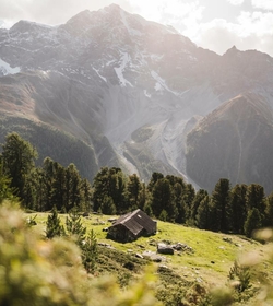 Eine kleine Berghütte liegt auf einer grünen Alm vor steilen Bergen im Meraner Land.